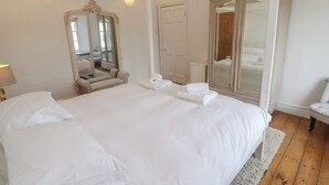 A large bed with white linens, a mirror, and a wardrobe in a hotel room. - Scillonia (Penzance)