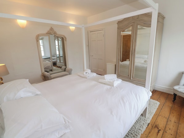 A large bed with white linens, a mirror, and a wardrobe in a hotel room. - Scillonia (Penzance)