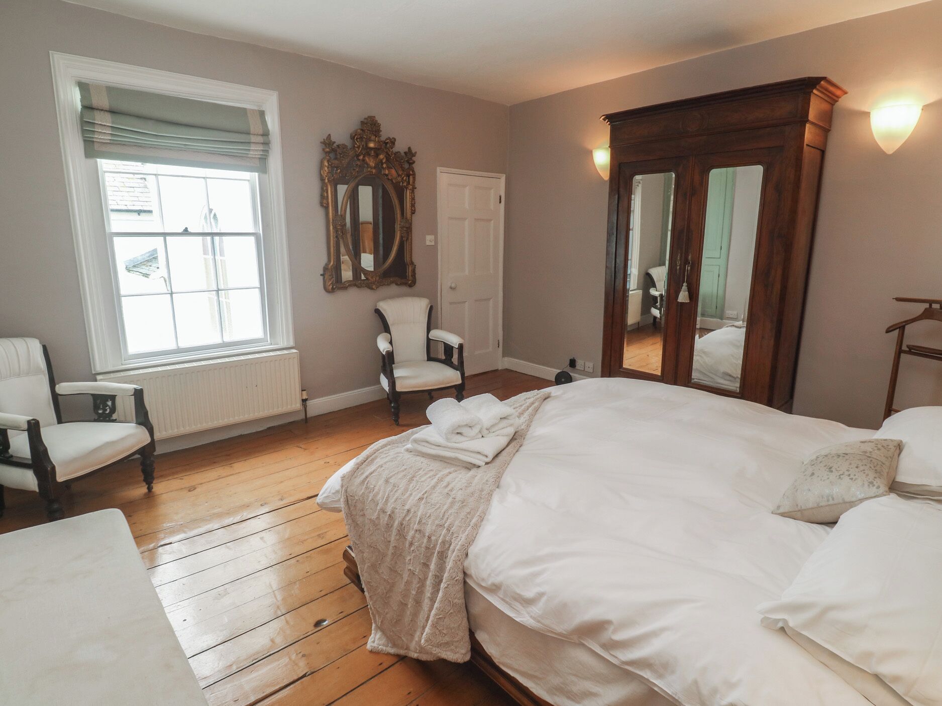 A bedroom with a large bed, a chair, a radiator, and a window with blinds.