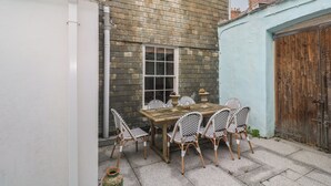 A patio with a wooden table and wicker chairs, a window, and a door. - Scillonia (Penzance)
