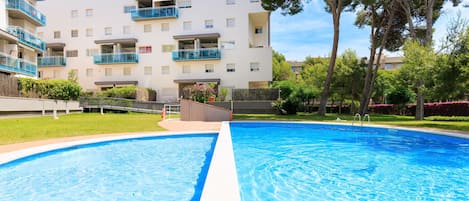 A swimming pool with a clear blue center, surrounded by a well-maintained lawn and trees.