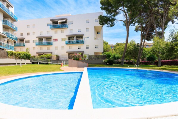 A swimming pool with a clear blue center, surrounded by a well-maintained lawn and trees.