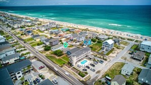 An aerial view of a coastal residential area with houses, a beach, and a large building with a swimming pool.