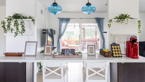 Una cocina con encimera blanca, dos lámparas colgantes azules, una cafetera roja y un calendario mostrando la fecha.