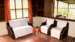 Ein Zimmer mit zwei Sofas, einem kleinen Tisch mit Obstschale und einem Fenster mit Vorhängen.