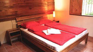 Ein hölzernes Bett mit roter Bettwäsche und ein Nachttisch mit einer Lampe.