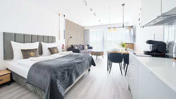 A modern hotel room with a large bed, a sofa, a dining area, and a kitchen.
