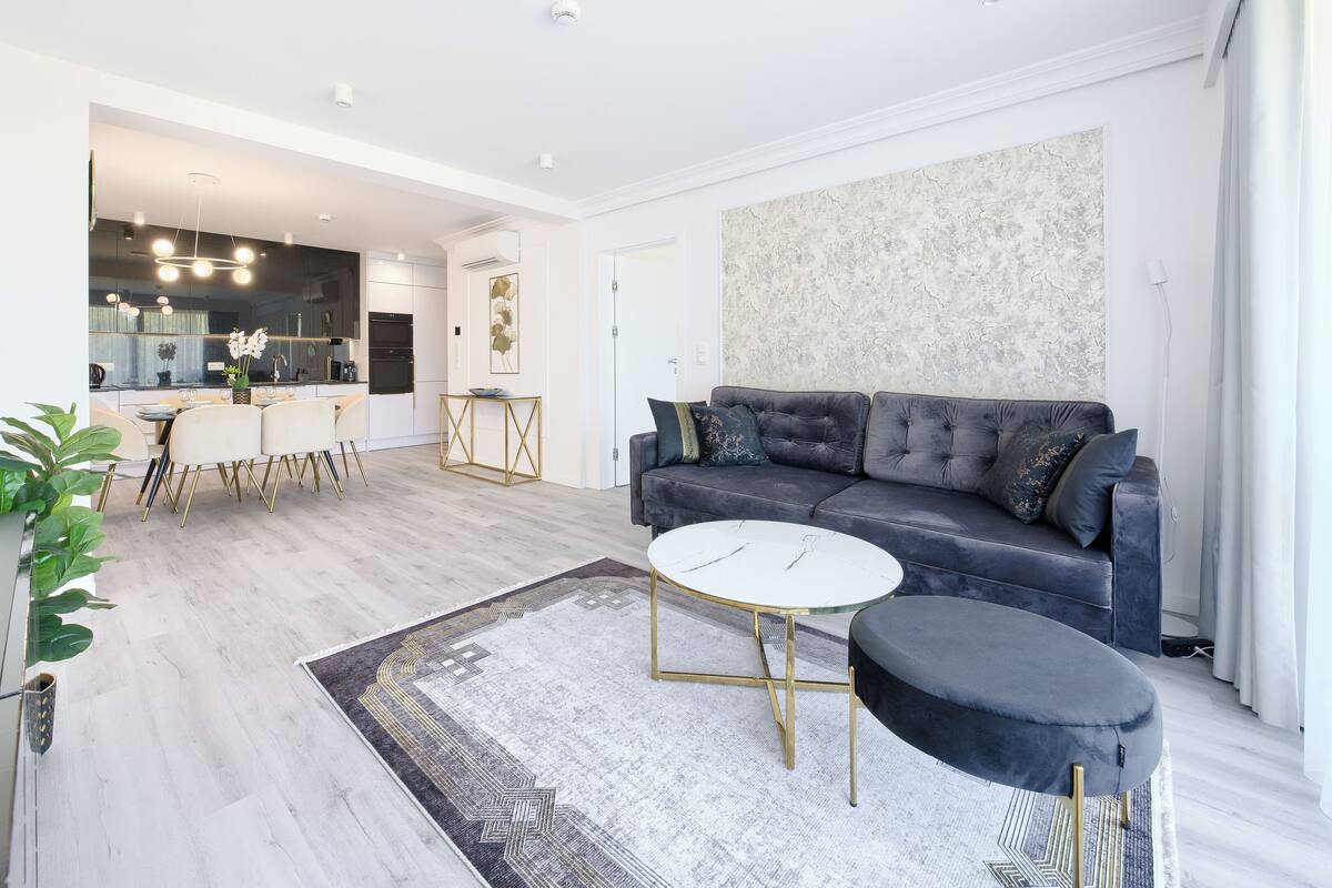 Een moderne woonkamer met een grijze bank, een witte salontafel en een kamerkleed met een patroon.