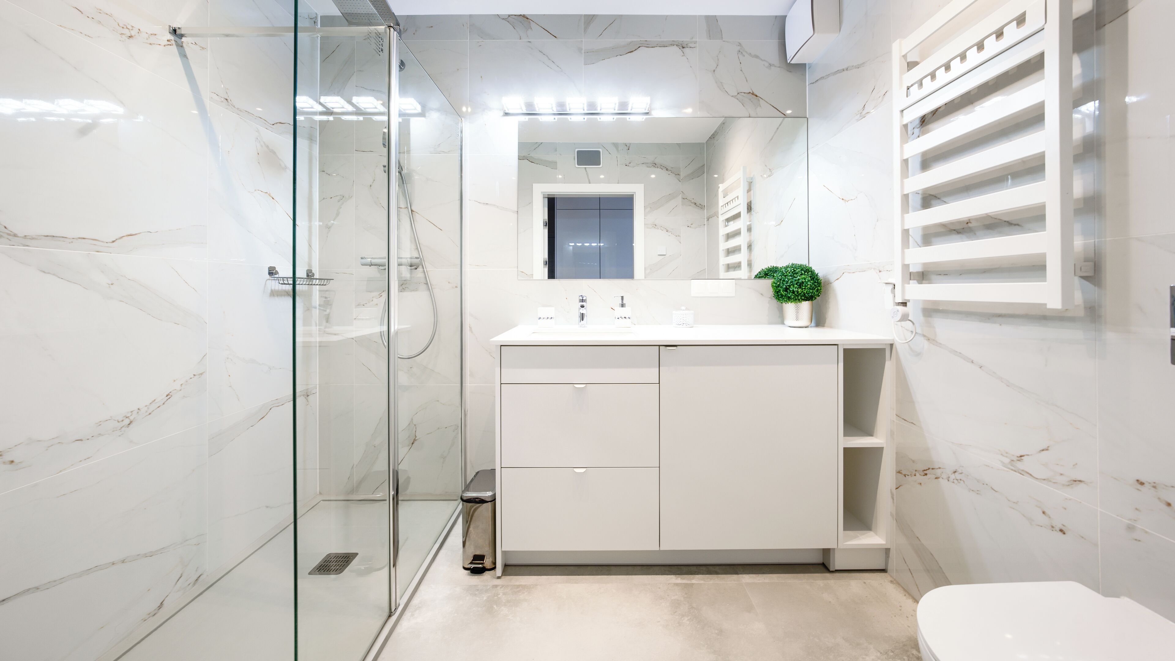 Ein modernes Badezimmer mit einer glasumrandeten Dusche, einem weißen Waschbecken mit einer kleinen Pflanze und Marmorwänden.