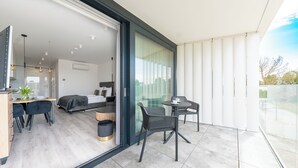 A modern hotel room with a balcony, a dining area, and a kitchen.