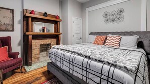 Un dormitorio con una cama grande, una chimenea, un sillón rojo y una pared con diseño floral.