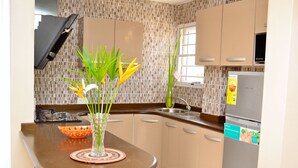 Una cocina con una mesa redonda, un florero con plantas, un cuenco y un refrigerador.