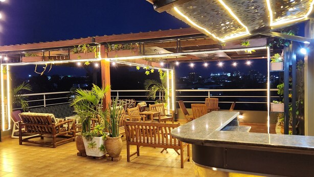 Un patio al aire libre con muebles de madera, plantas en macetas y luces colgantes.