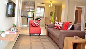 Una sala de estar moderna con un sofá, un sillón rojo, una mesa de centro y un televisor montado en la pared.