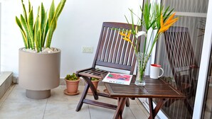Una silla de madera con una revista, una planta en maceta y un florero con flores en un balcón.