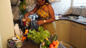 Una cocina con una mujer preparando comida, un fregadero, armarios y diversos utensilios de cocina.