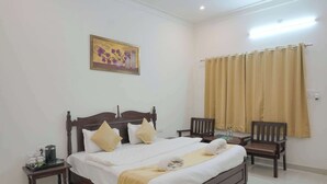 A hotel room with a wooden bed, bedside tables, a chair, a painting, and a window with curtains. - Akshay valley Hotel & Restro (Udaipur)