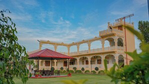 A traditional building with a red-roofed pavilion, multiple balconies, and a well-maintained lawn. - Akshay valley Hotel & Restro (Udaipur)