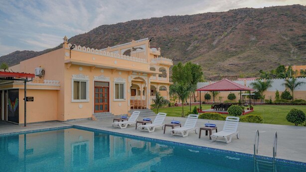A pool area with lounge chairs and a building with traditional architecture. - Akshay valley Hotel & Restro (Udaipur)