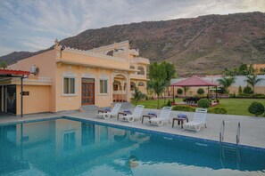 A pool area with lounge chairs and a building with traditional architecture. - Akshay valley Hotel & Restro (Udaipur)