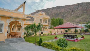 A building with a traditional architectural style, a covered outdoor seating area, and a view of a mountainous landscape. - Akshay valley Hotel & Restro (Udaipur)