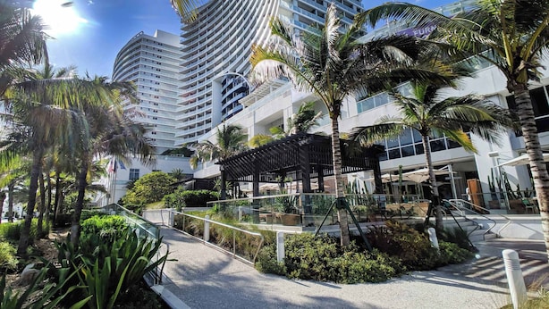 Een modern hotel met een gebogen gevel, omringd door palmbomen en een verzorgde tuin.