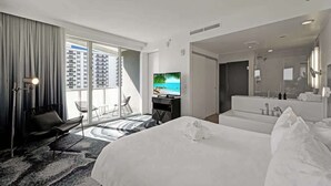 Een moderne hotelkamer met een groot bed, een televisie, een bureau en een badkamer met spiegel en wastafel.