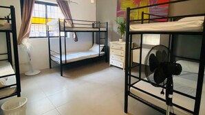 Een studentenkamer met stapelbedden, een plafondventilator, een raam met gordijnen, een witte dressoir en een kleurrijk abstract schilderij aan de muur.