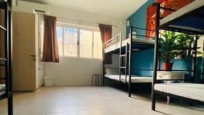 Een slaapkamer met stapelbedden, een plafondventilator, een raam met gordijnen en een kamerplant.