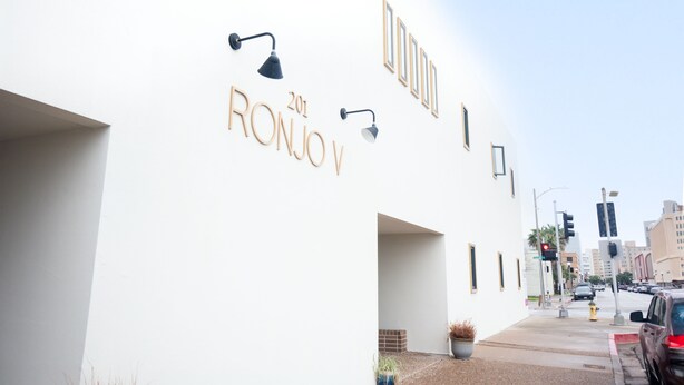 Un bâtiment à la façade blanche, portant l’inscription « RONJOY 201 » en lettres dorées, et deux appliques murales noires.