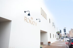 A building with a white facade, the name "RONJOY 201" in gold lettering, and two black wall-mounted lights.