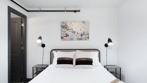 Une chambre à coucher avec un lit, deux tables de chevet, une commode, un tableau au mur et une porte.