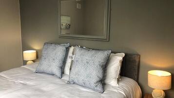 A neatly made bed with patterned pillows, a bedside lamp, and a framed mirror on the wall.