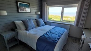 Un dormitorio con cama, mesita de noche, escritorio y ventana con vistas.