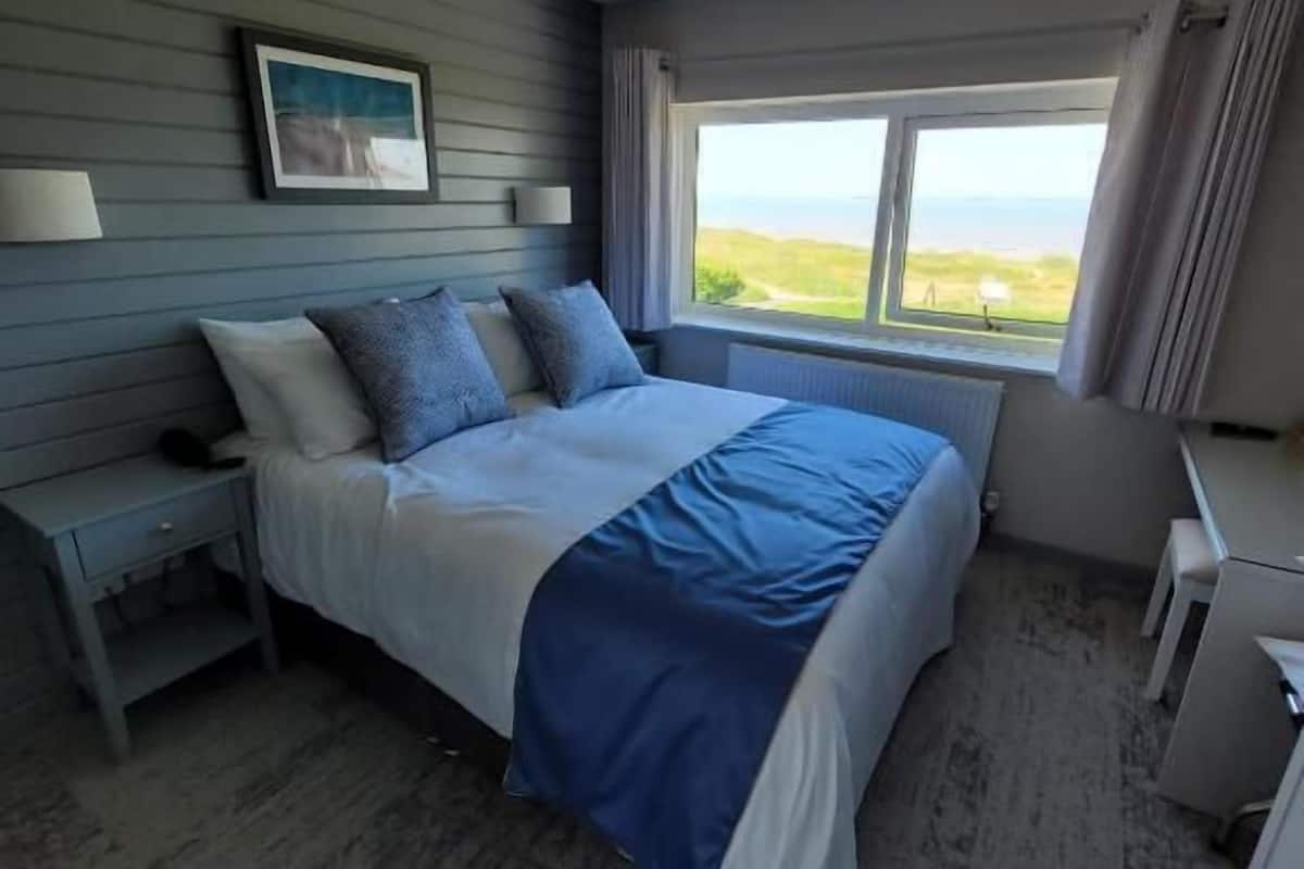 Un dormitorio con cama, mesita de noche, escritorio y ventana con vistas.