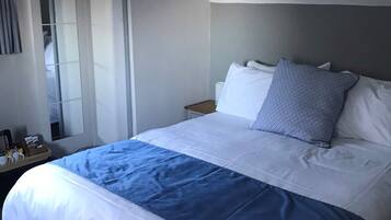 A hotel room with a large bed, a nightstand, a mirror, and a ceiling light.