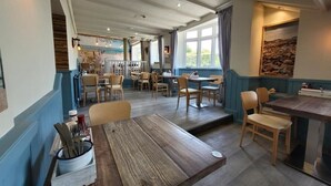 Un restaurante con mesas y sillas de madera, una zona de bar y vistas al exterior.