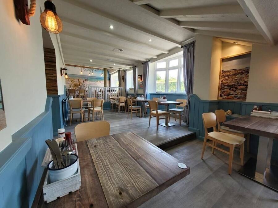 A restaurant with wooden tables and chairs, a bar area, and a view of the outdoors.