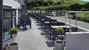 Un patio al aire libre con mesas y sillas, plantas en macetas y vistas a una colina.