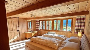 A wooden cabin bedroom with a large bed, a bedside table with a lamp, and a window with curtains. - Wohnung Lake View (Schwanden bei Brienz)