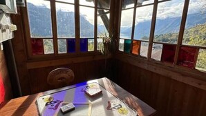 A corner room with a table and chairs, large windows with a mountain view, and a wooden ceiling. - Wohnung Lake View (Schwanden bei Brienz)