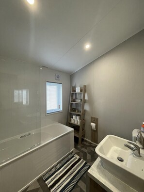 Een moderne badkamer met een badkuip, wastafel en een plank met toiletartikelen.