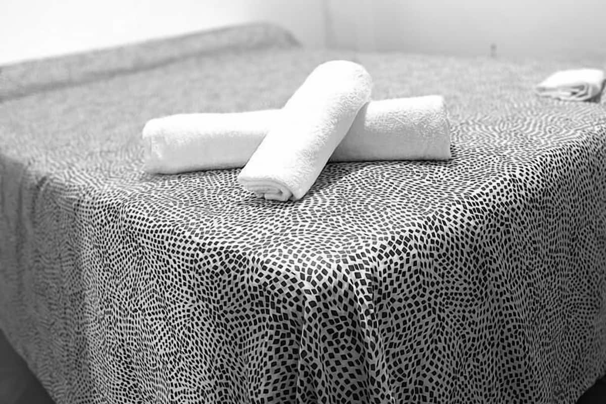 A bed with a patterned bedspread and two rolled towels on it.
