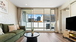 Una sala moderna con un sofá verde, una mesa de centro redonda y un televisor de pantalla plana sobre un soporte de madera.