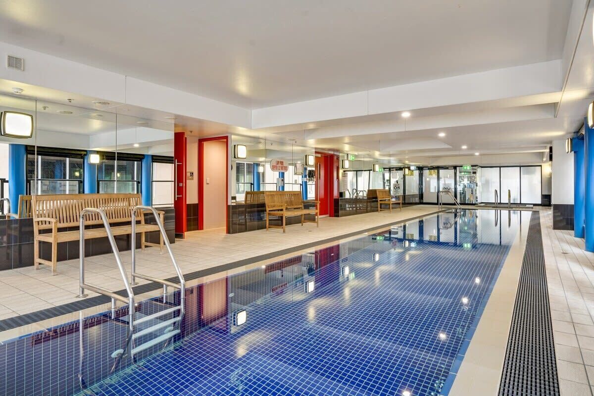 A swimming pool with a tiled floor, benches, and a changing room area.