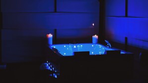 Una stanza scarsamente illuminata con una vasca idromassaggio illuminata di blu e due candele.