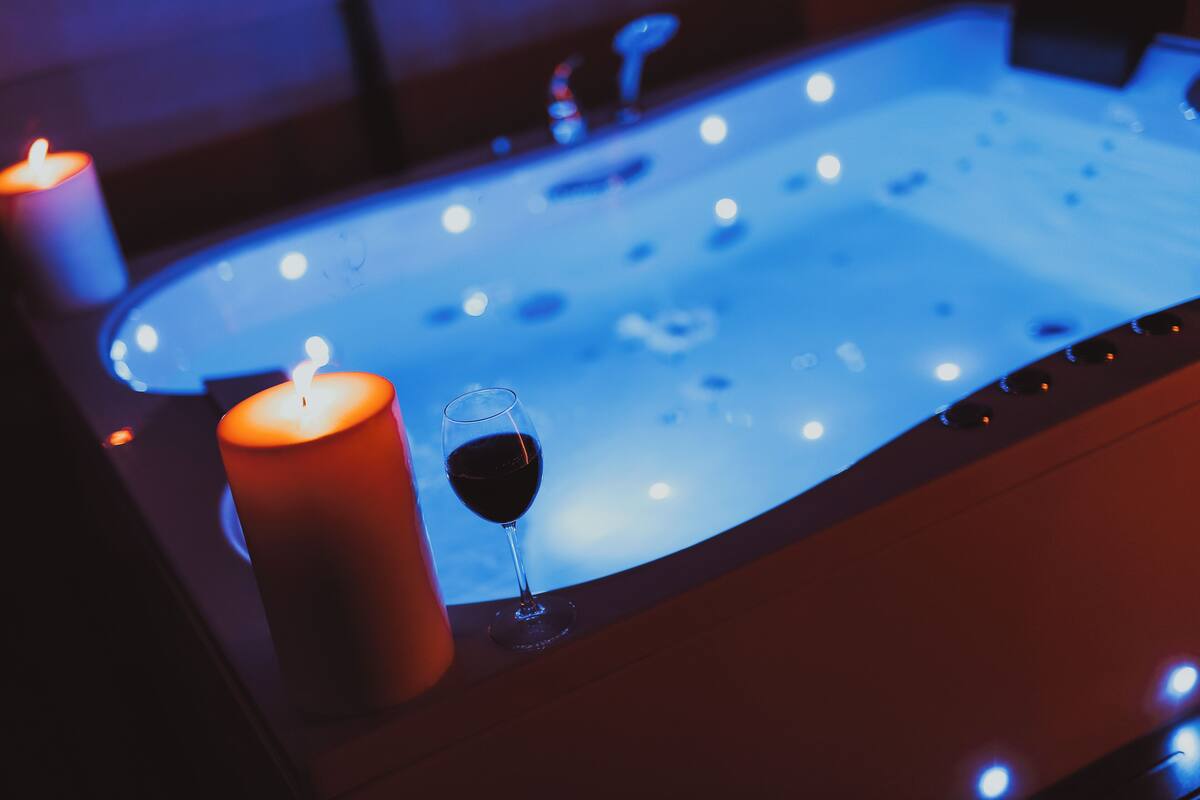 Una bañera con luz azul, una vela y una copa de vino tinto.