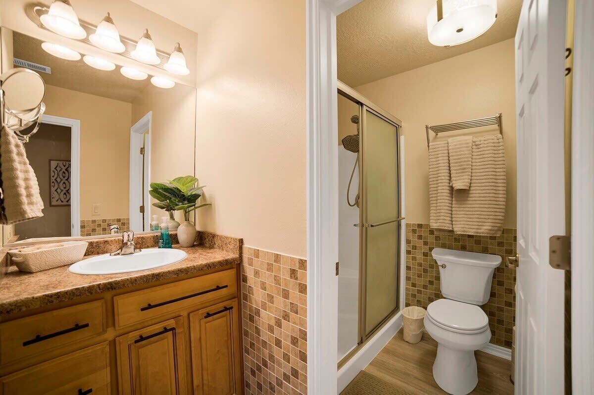 A bathroom with a sink, mirror, towel rack, shower, and toilet.