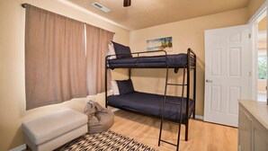 Una cama individual superpuesta con ventilador de techo, un sofá, una puerta y un cuadro en la pared.