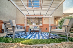 An outdoor patio with two grey chairs, a small table, and a blue striped rug.